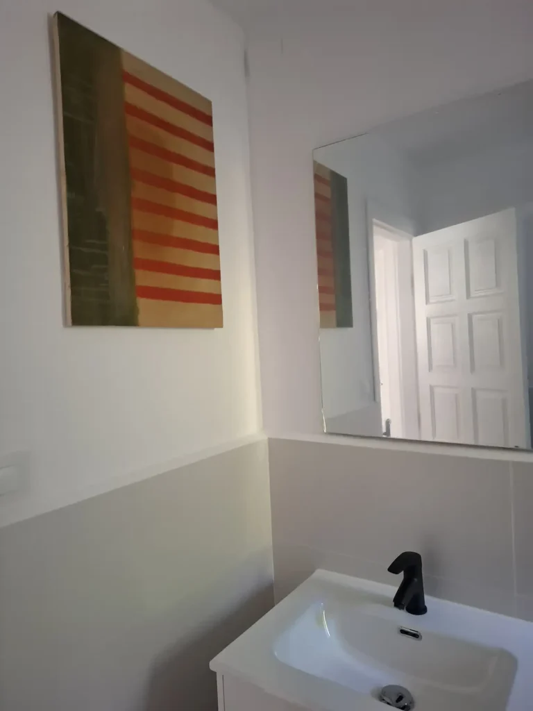 Un lavabo bajo un espejo con un cuadro decorativo