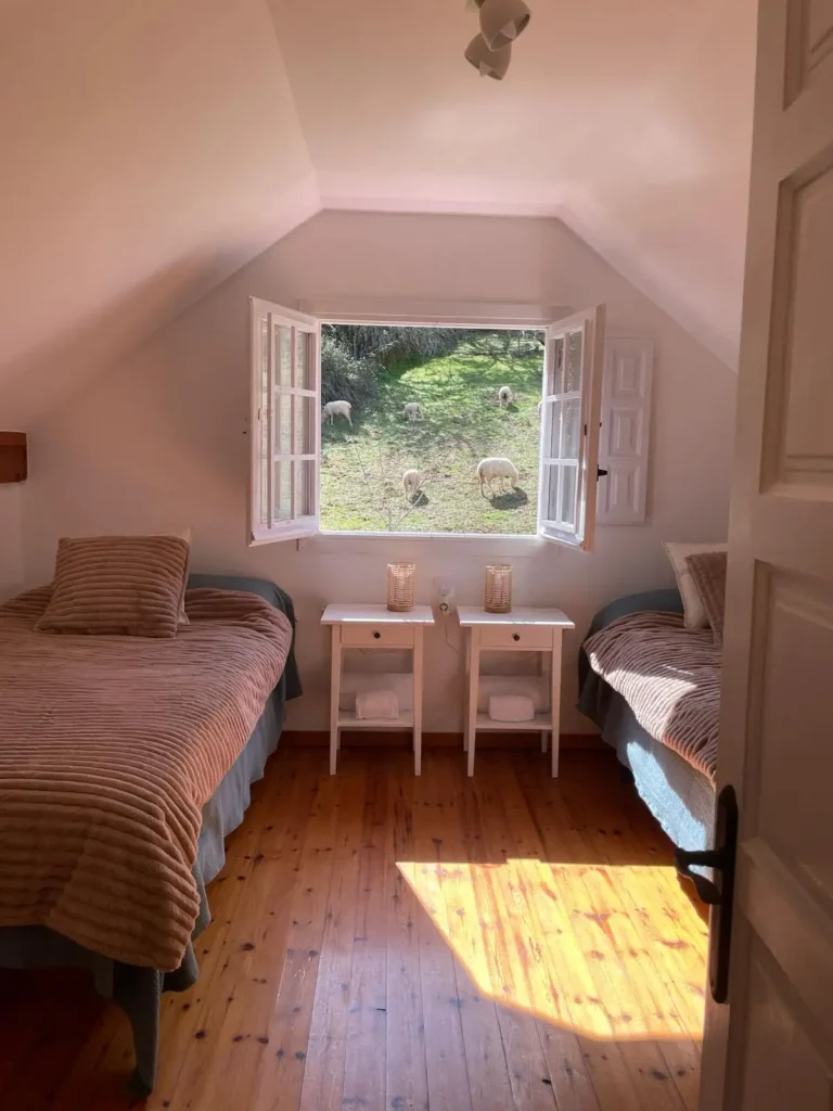 Una habitación abuardillada con dos camas. Por la ventana se ven ovejas.