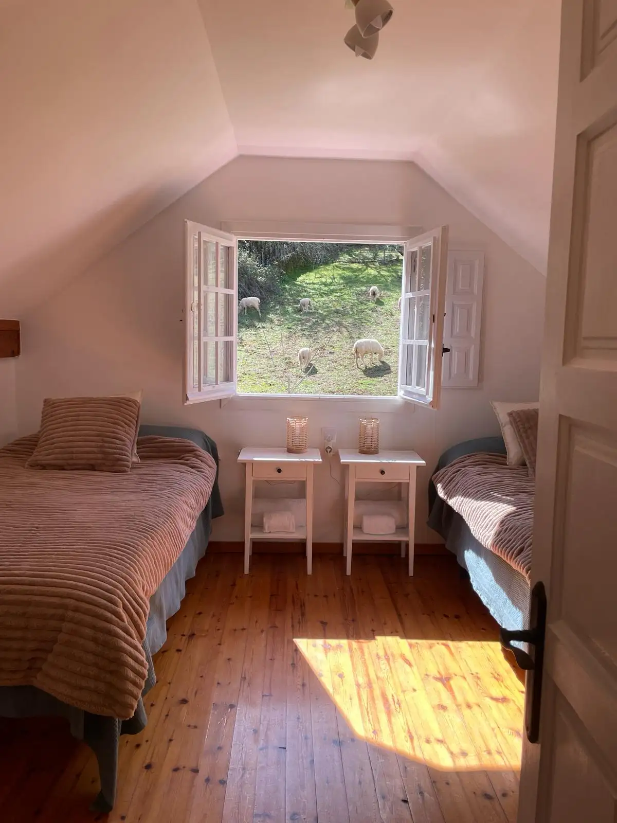 Una habitación abuardillada con dos camas. Por la ventana se ven ovejas.