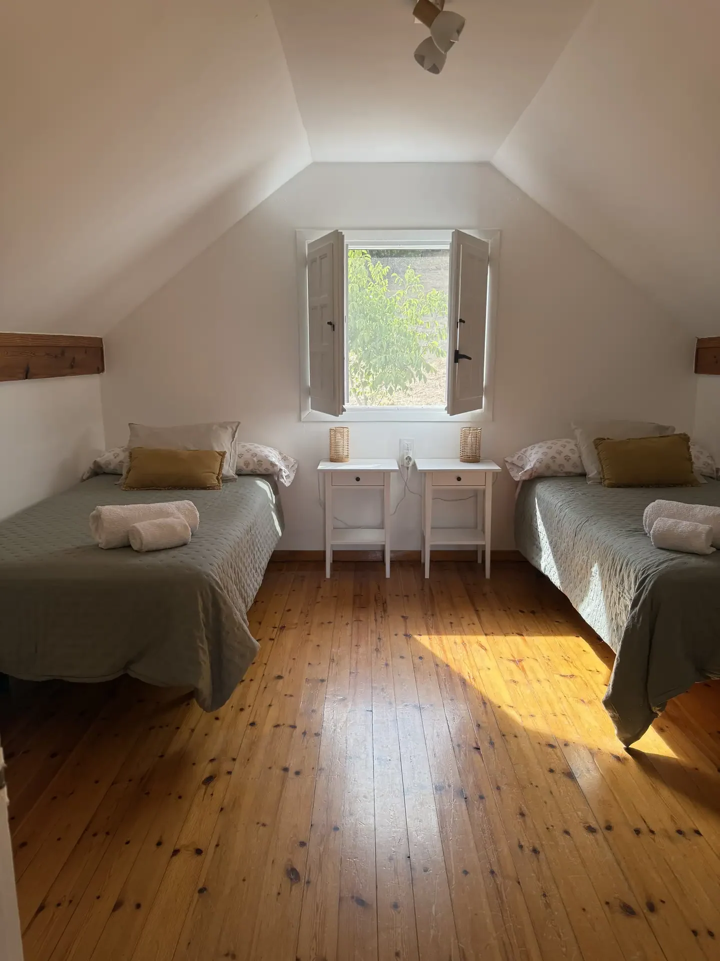 Habitación abuhardillada con dos camas y una ventana en el centro
